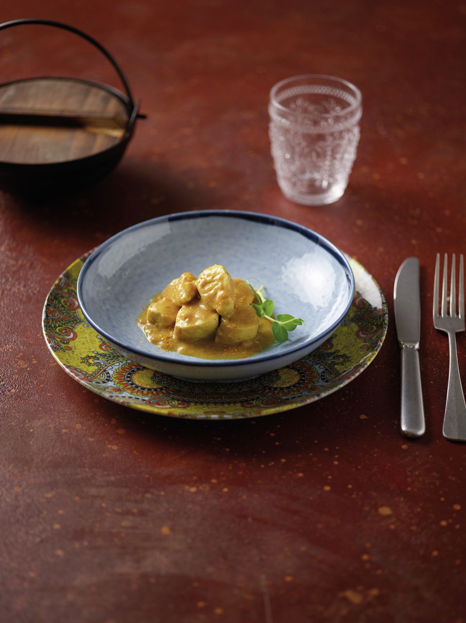 Vogelperspektive auf ein Tellerset mit Mandala-Muster, bestehend aus einem blauen Schüssel auf einem dekorativen Teller, serviert mit einem Currygericht.