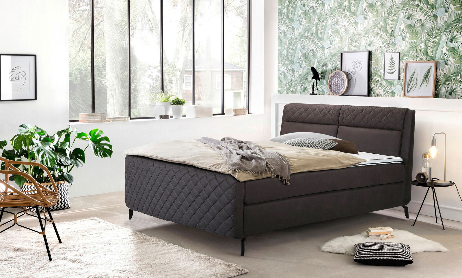 Boxspringbett in einem modernen Schlafzimmer mit großen Fenstern, Pflanzen und stilvoller Dekoration, seitliche Perspektive