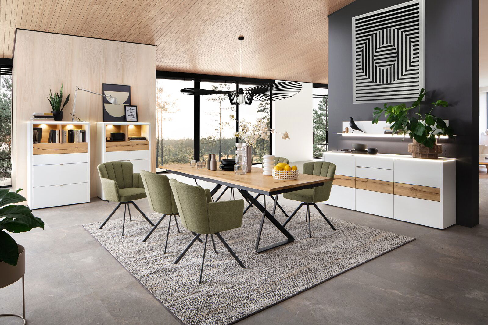 Venjakob Wand-Paneel GAME Moderne Esszimmer-Einrichtung mit grün gepolsterten Stühlen, Holztisch und beleuchteten Vitrinen, seitliche Perspektive.