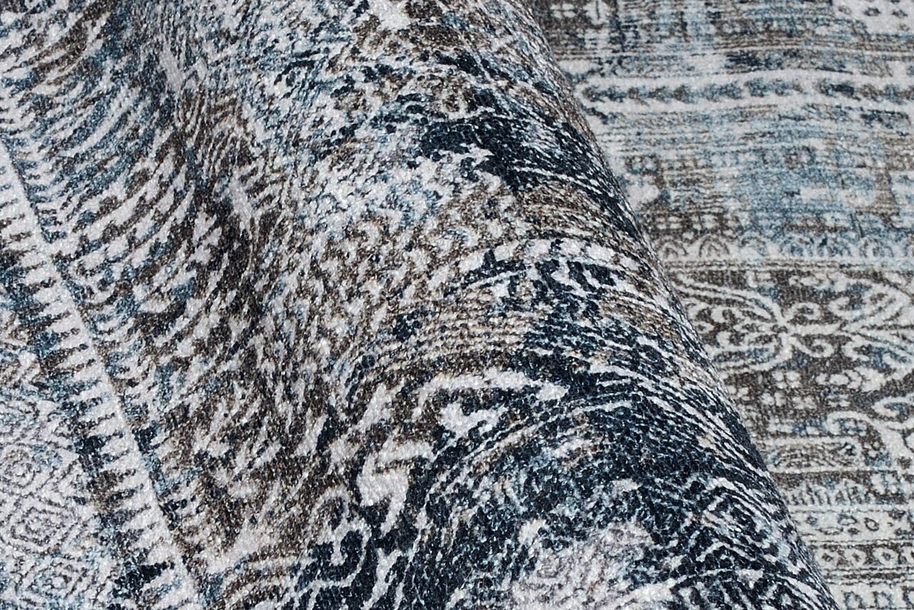 Nahaufnahme eines gemusterten Teppichs in Blau- und Brauntönen, perspektivisch von der Seite aufgenommen.