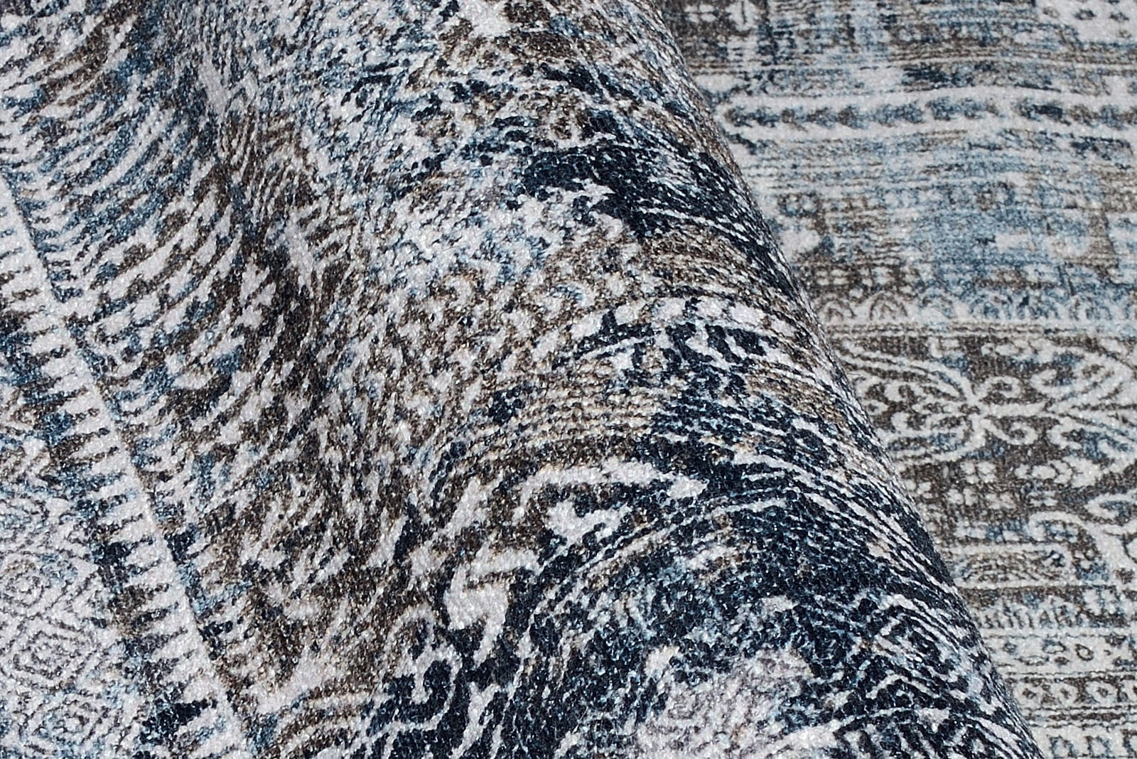 Nahaufnahme eines gemusterten Teppichs in Blau- und Brauntönen, perspektivisch von der Seite aufgenommen.