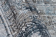 Nahaufnahme eines gemusterten Teppichs in Blau- und Brauntönen, perspektivisch von der Seite aufgenommen.