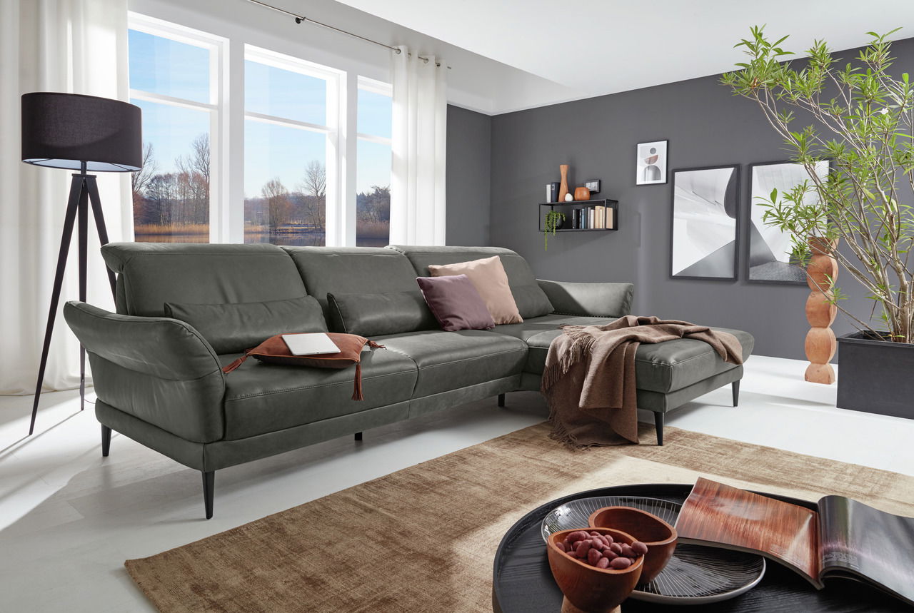 Graue Longchairkombination in modernem Wohnzimmer mit großen Fenstern, Pflanzen und stilvollen Dekorationen, seitliche Perspektive.