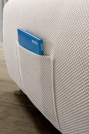 Nahaufnahme einer strukturierten, cremefarbenen Sofaecke mit einer praktischen Seitentasche, die ein blaues Buch enthält, auf einem Holzboden.