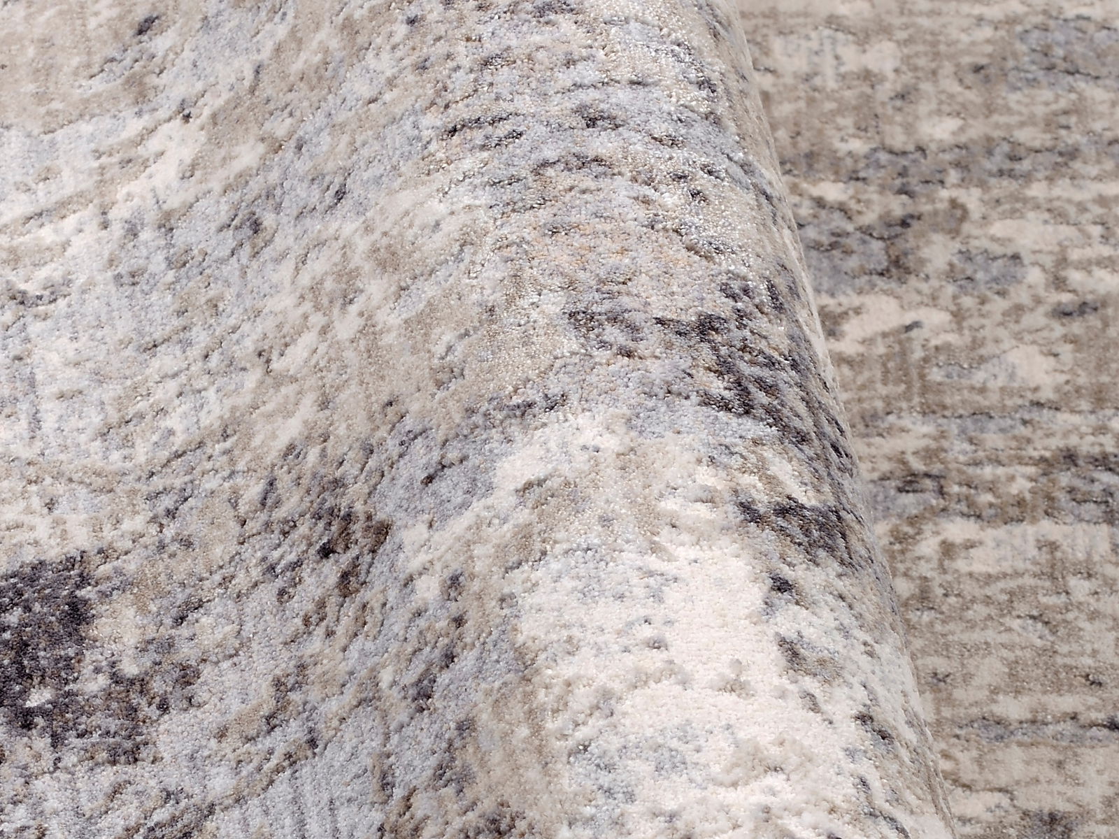 Nahaufnahme eines Designer Teppichs mit abstraktem Muster in Grau- und Beigetönen, perspektivisch von der Seite aufgenommen.