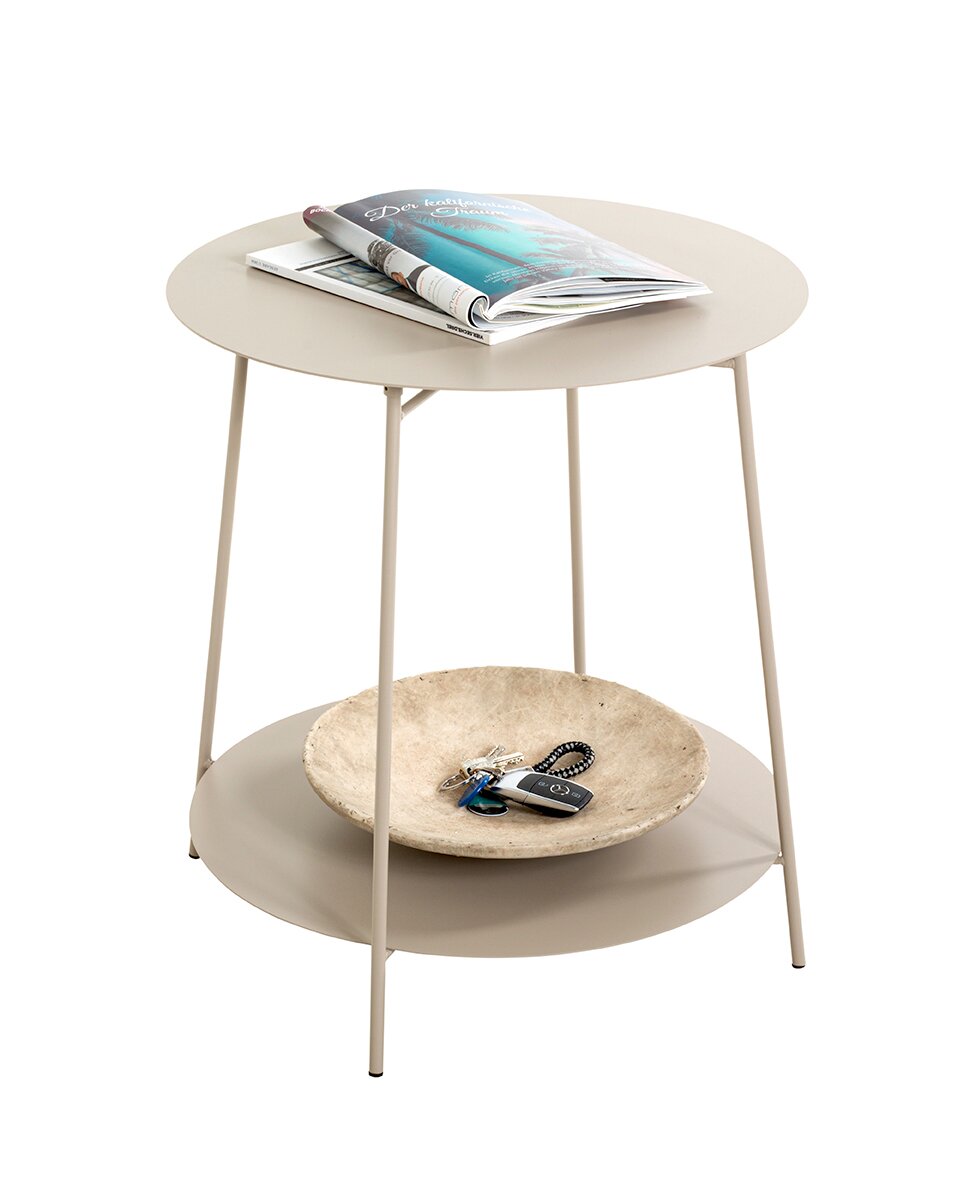 Runder, zweistöckiger Beistelltisch in Beige mit schlanken Metallbeinen; auf der oberen Platte liegen Magazine, auf der unteren Ablage eine Schale mit Schlüssel und Autoschlüssel, fotografiert in leicht schräger Vorderansicht vor weißem Hintergrund.