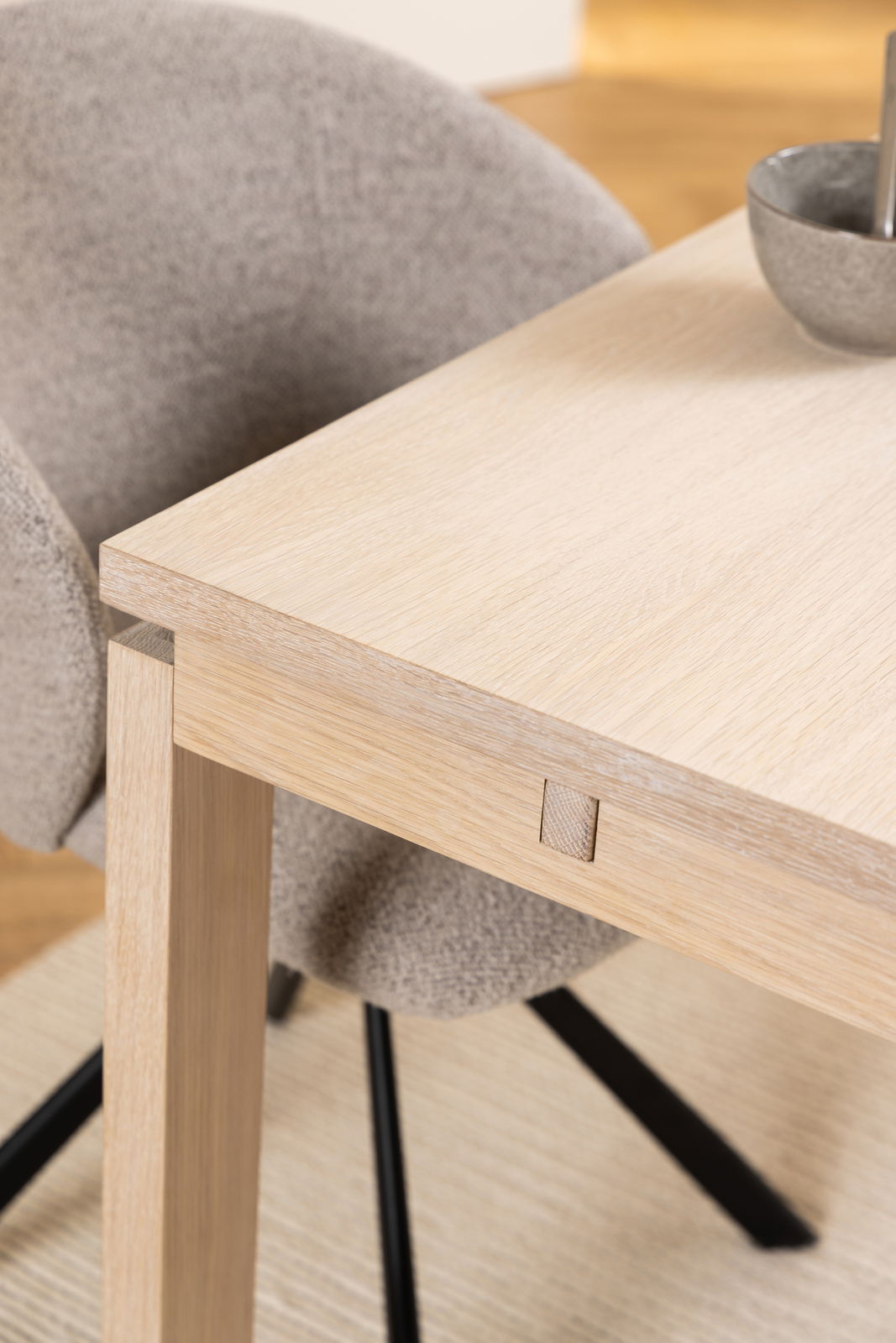 Nahaufnahme eines modernen Esstisches aus hellem Holz mit einem grauen Stuhl im Hintergrund, seitliche Perspektive.