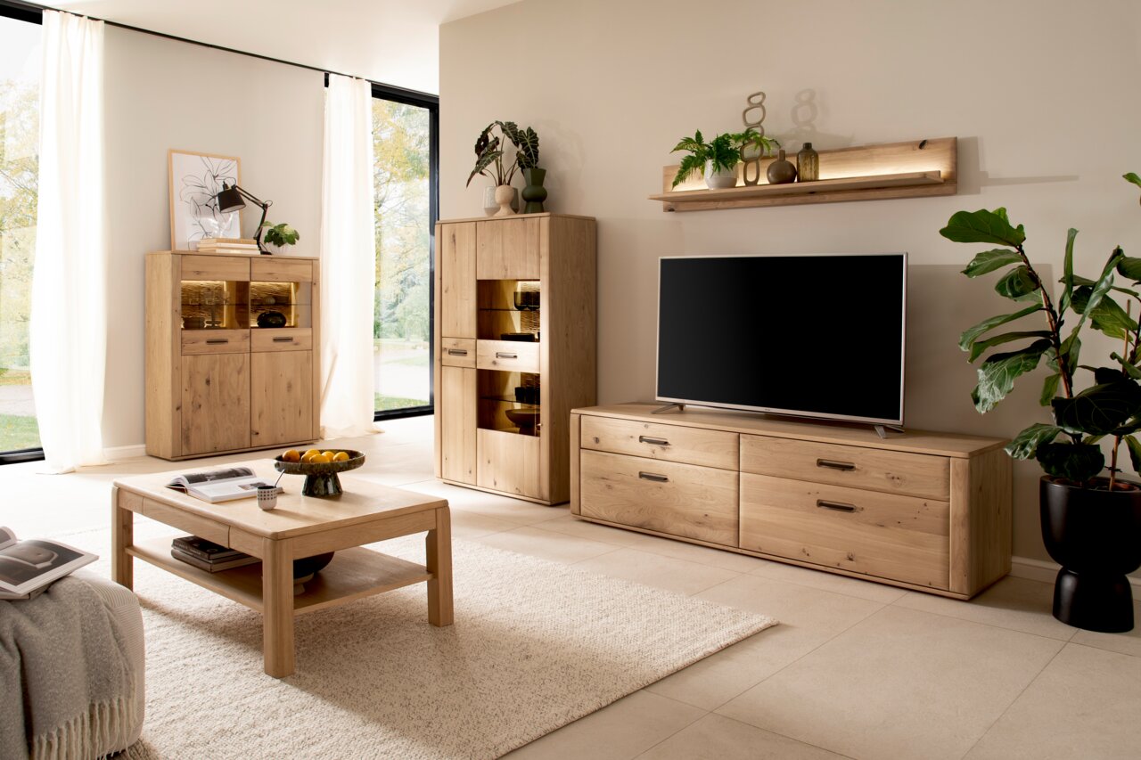 Wohnzimmer mit modernen Holzmöbeln, darunter ein TV-Element, ein Highboard und ein Wandboard, aus hellem Holz. Perspektive von vorne.