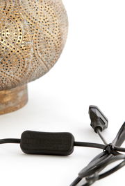 Nahaufnahme eines dekorativen Lampenfußes mit filigranem Muster und einem schwarzen Kabel mit Schalter, seitliche Perspektive.