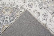 Nahaufnahme eines dekorativen Teppichs mit floralen Mustern in Beige- und Grautönen, teilweise umgeschlagen, um die Rückseite zu zeigen.