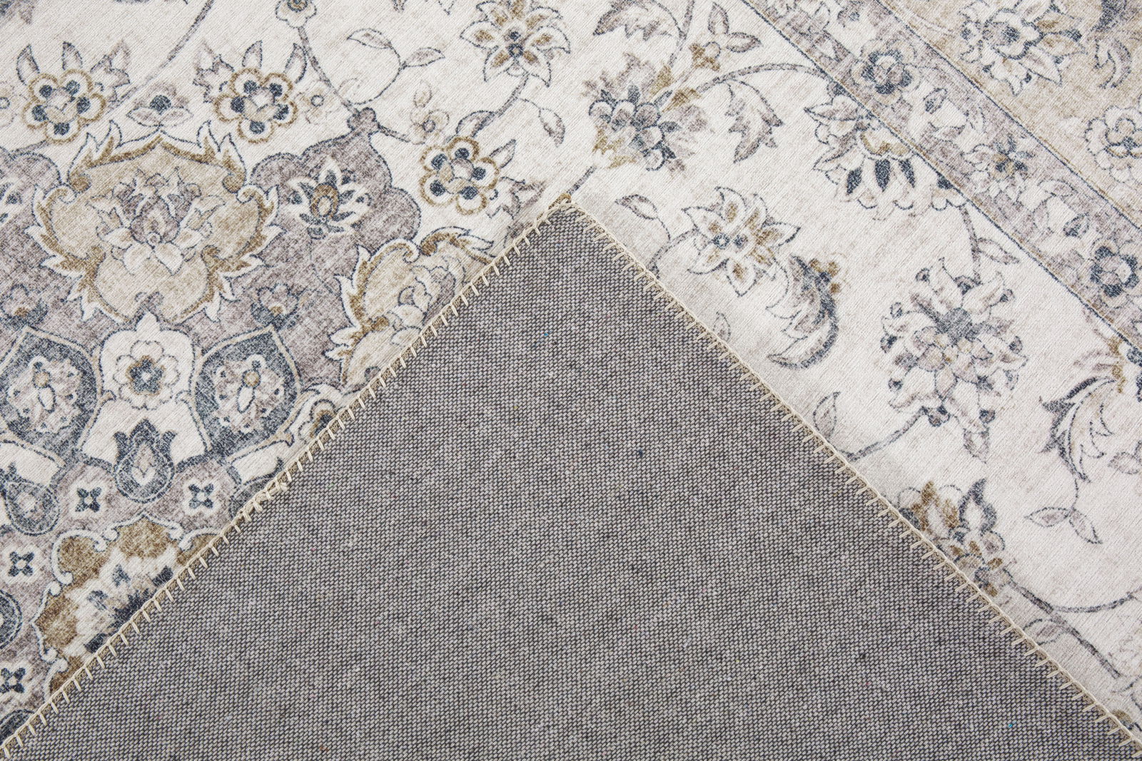 Nahaufnahme eines dekorativen Teppichs mit floralen Mustern in Beige- und Grautönen, teilweise umgeschlagen, um die Rückseite zu zeigen.