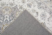 Nahaufnahme eines dekorativen Teppichs mit floralen Mustern in Beige- und Grautönen, teilweise umgeschlagen, um die Rückseite zu zeigen.