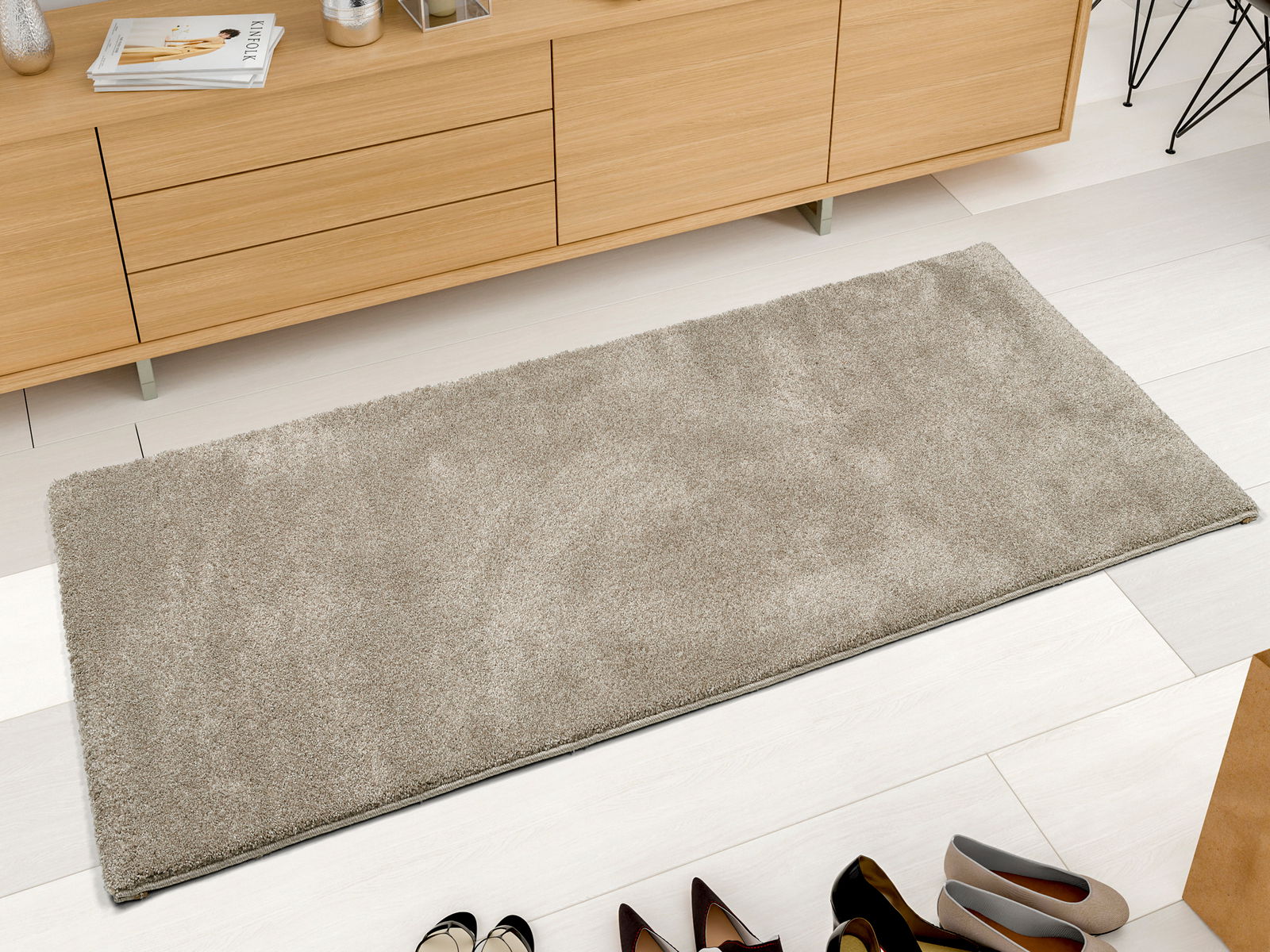 Beige Uni-Teppich in rechteckiger Form, aus der Vogelperspektive fotografiert, auf hellem Holzboden vor einem Sideboard platziert.