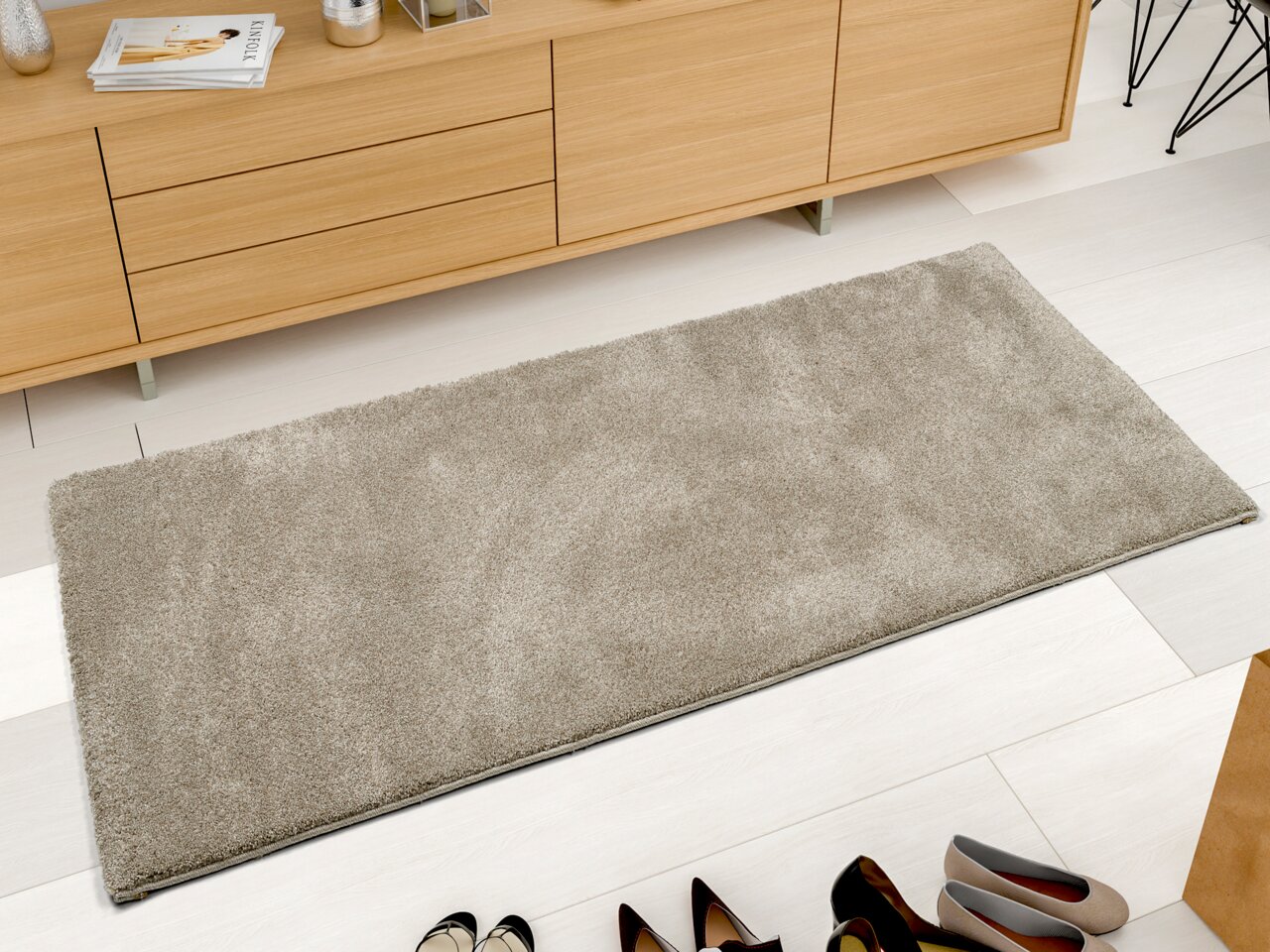 Beige Uni-Teppich in rechteckiger Form, aus der Vogelperspektive fotografiert, auf hellem Holzboden vor einem Sideboard platziert.