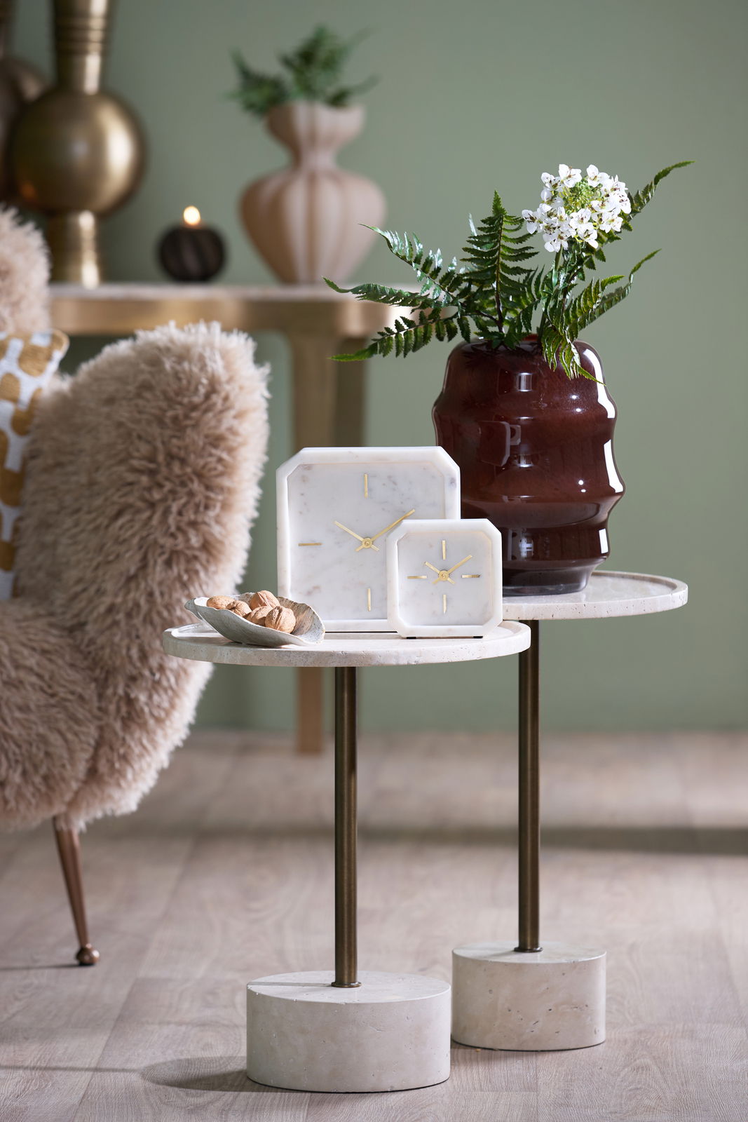 Light&Living Uhr PABLIA Zwei elegante Uhren aus Marmor mit goldenen Zeigern auf einem stilvollen Beistelltisch, umgeben von einer dekorativen Vase und einem gemütlichen Sessel. Perspektive: seitlich.