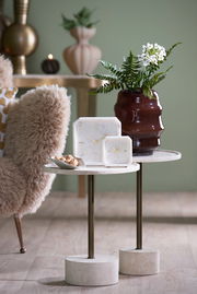 Zwei elegante Uhren aus Marmor mit goldenen Zeigern auf einem stilvollen Beistelltisch, umgeben von einer dekorativen Vase und einem gemütlichen Sessel. Perspektive: seitlich.