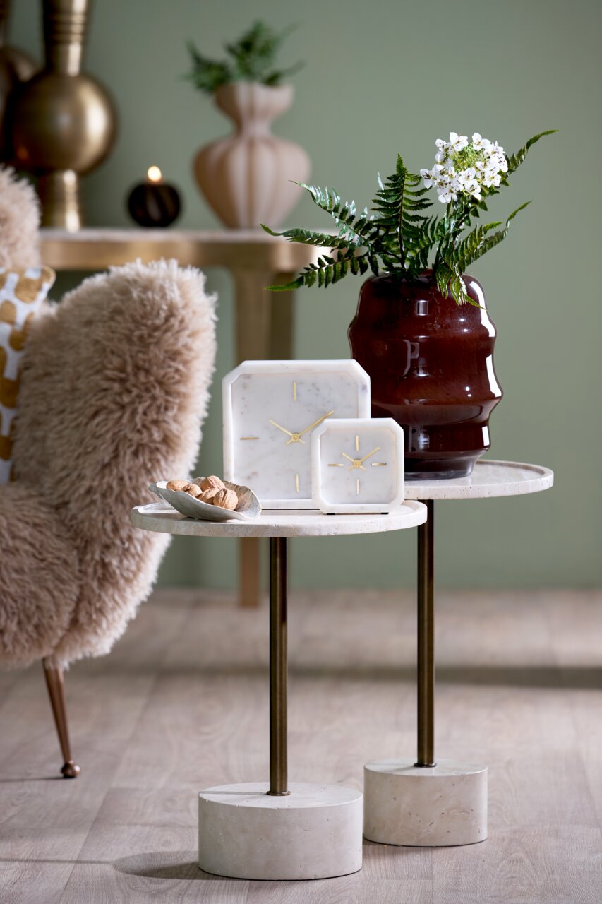 Light&Living Uhr PABLIA Zwei elegante Uhren aus Marmor mit goldenen Zeigern auf einem stilvollen Beistelltisch, umgeben von einer dekorativen Vase und einem gemütlichen Sessel. Perspektive: seitlich.