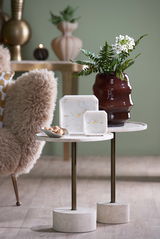 Zwei elegante Uhren aus Marmor mit goldenen Zeigern auf einem stilvollen Beistelltisch, umgeben von einer dekorativen Vase und einem gemütlichen Sessel. Perspektive: seitlich.