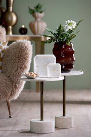 Zwei elegante Uhren aus Marmor mit goldenen Zeigern auf einem stilvollen Beistelltisch, umgeben von einer dekorativen Vase und einem gemütlichen Sessel. Perspektive: seitlich.