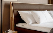 Nahaufnahme eines Boxspringbetts mit braunem Kopfteil und weißen Kissen, seitliche Perspektive