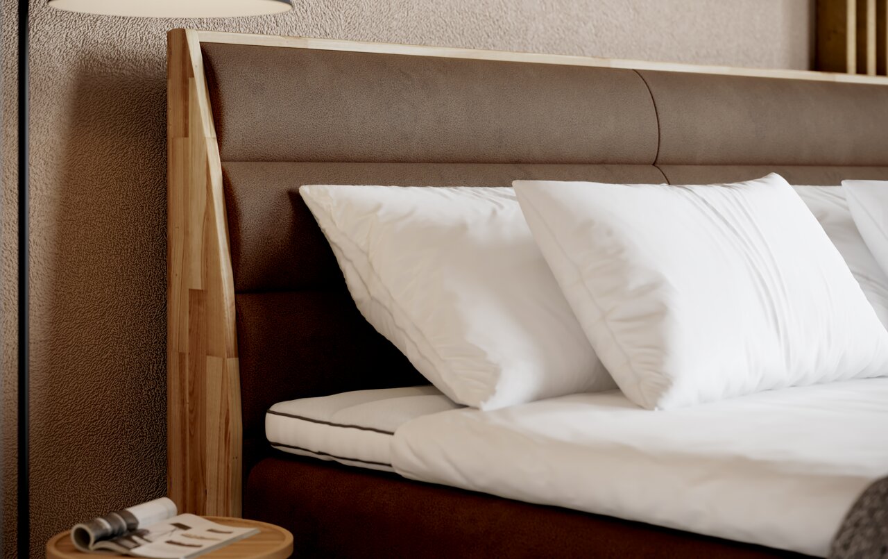 Close-up van een boxspringbed met een bruin hoofdeinde en witte kussens, gezien vanaf de zijkant