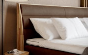 Close-up van een boxspringbed met een bruin hoofdeinde en witte kussens, gezien vanaf de zijkant