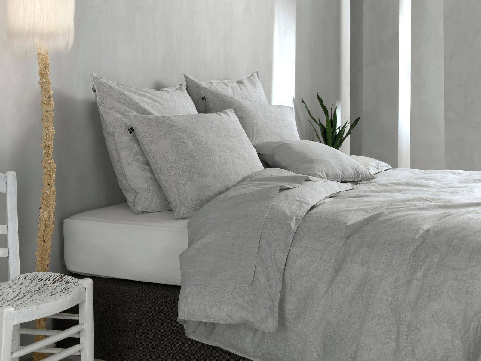 Graue Bettwäsche mit Paisley-Muster auf einem Bett, seitliche Perspektive