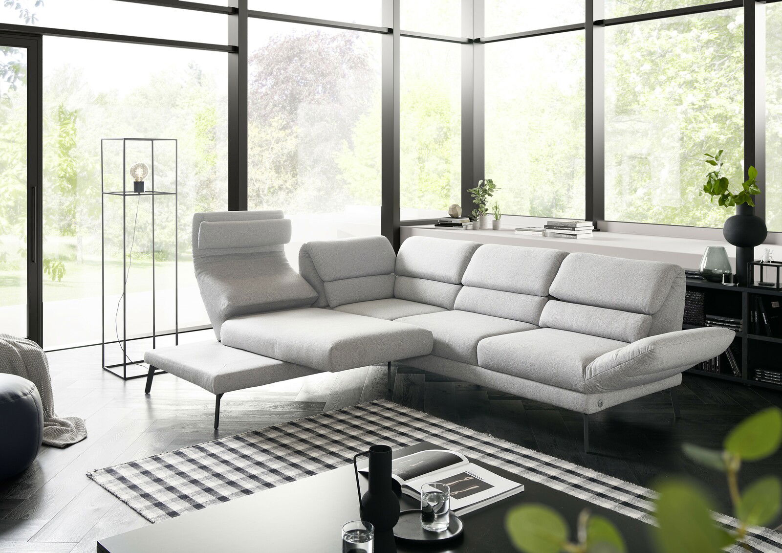 Moderne graue Eckgarnitur in einem hellen Wohnzimmer mit großen Fenstern, seitliche Perspektive.