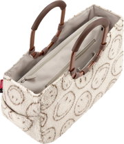 Beige Handtasche aus flauschigem Teddy-Material mit kreisförmigem Muster, braunen Tragegriffen und innenliegendem Reißverschlussfach, in schräger Draufsicht von oben vorn.
