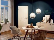 Zwei moderne, kugelförmige Pendelleuchten hängen von der Decke in einem stilvoll eingerichteten Wohnzimmer. Die Perspektive zeigt die Leuchten von der Seite, mit einem Esstisch und Stühlen im Vordergrund.