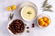 Draufsicht auf eine Schale mit cremiger Suppe, garniert mit Birnenscheiben und Thymian, umgeben von Birnen, Kastanien und Orangen auf hellem Hintergrund