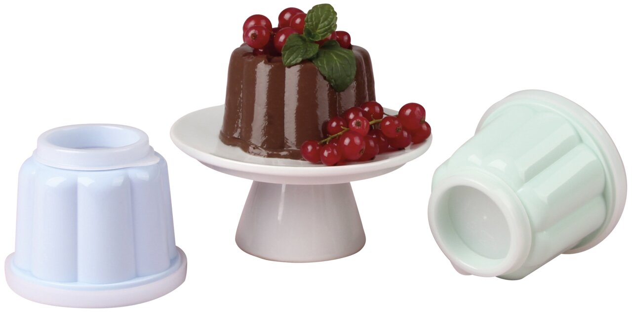 Drei Puddingformen in verschiedenen Farben, eine mit Schokoladenpudding und roten Johannisbeeren gefüllt, aus seitlicher Perspektive.
