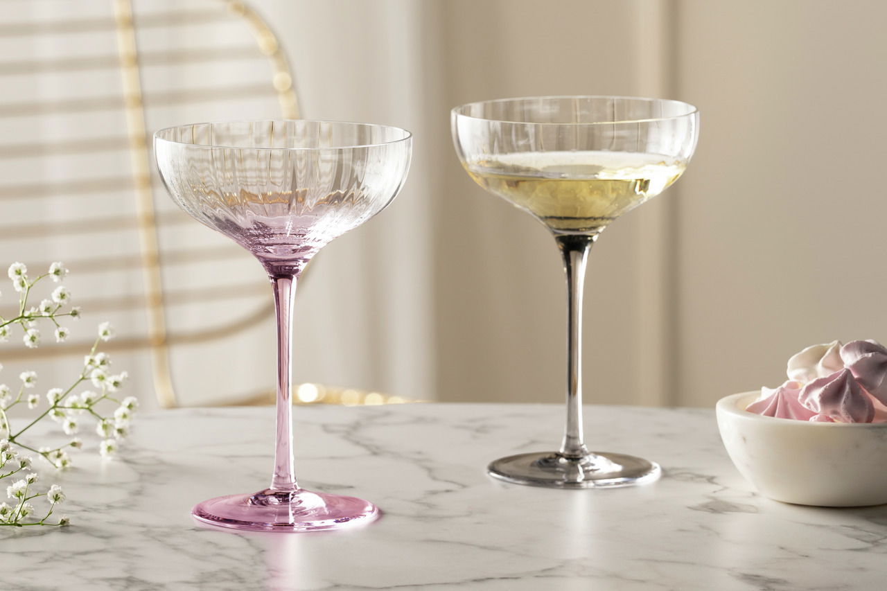 Leonardo Champagnerschale POESIA grau POESIA Zwei elegante Champagnerschalen auf einem Marmortisch, eine in Rosa und eine in Grau, mit einer seitlichen Perspektive.