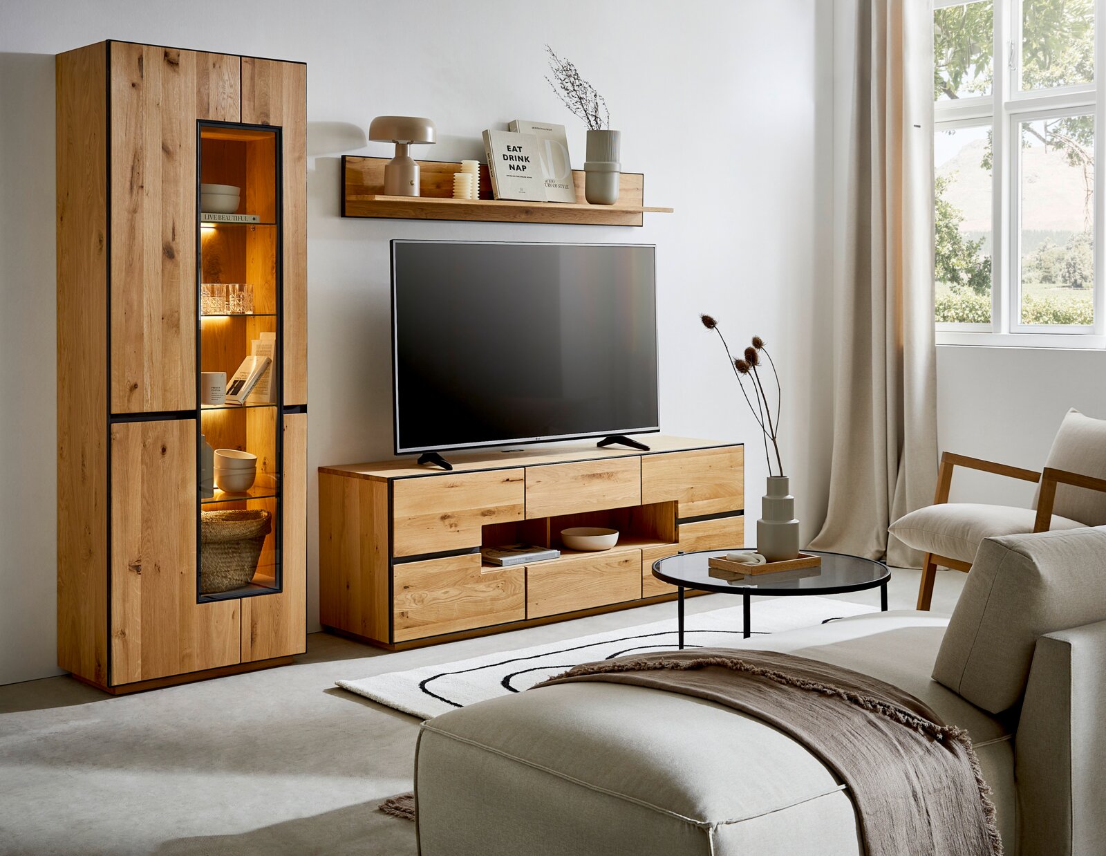 Moderne woonkamer met houten tv-meubel en hoge vitrinekast met glazen deur en warme LED-verlichting, frontaal aanzicht in een licht interieur met tv en wandplank.