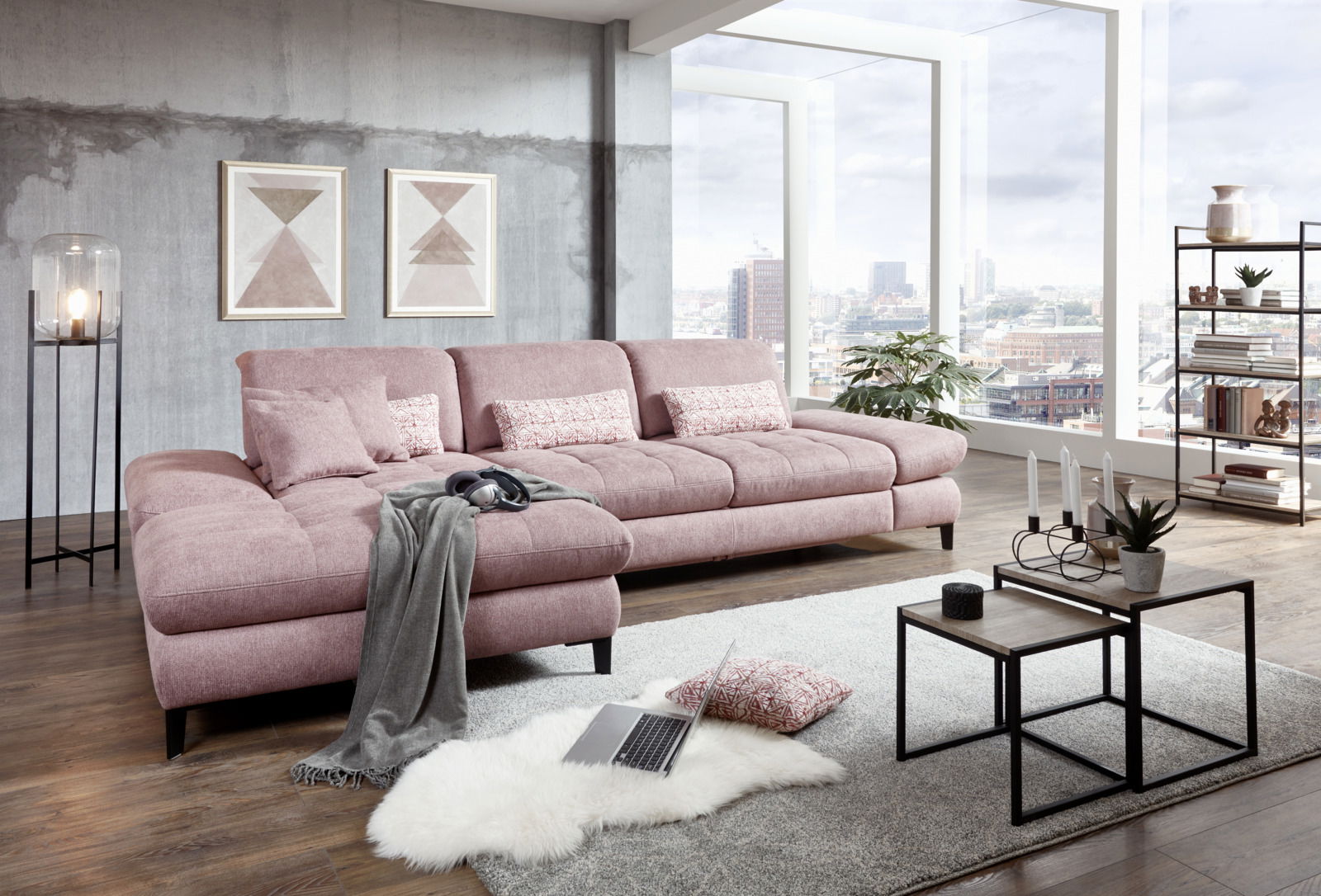 Großes, modernes Ecksofa in Rosa mit Kissen, in einem stilvollen Wohnzimmer mit großen Fenstern und Stadtblick, aus seitlicher Perspektive fotografiert.