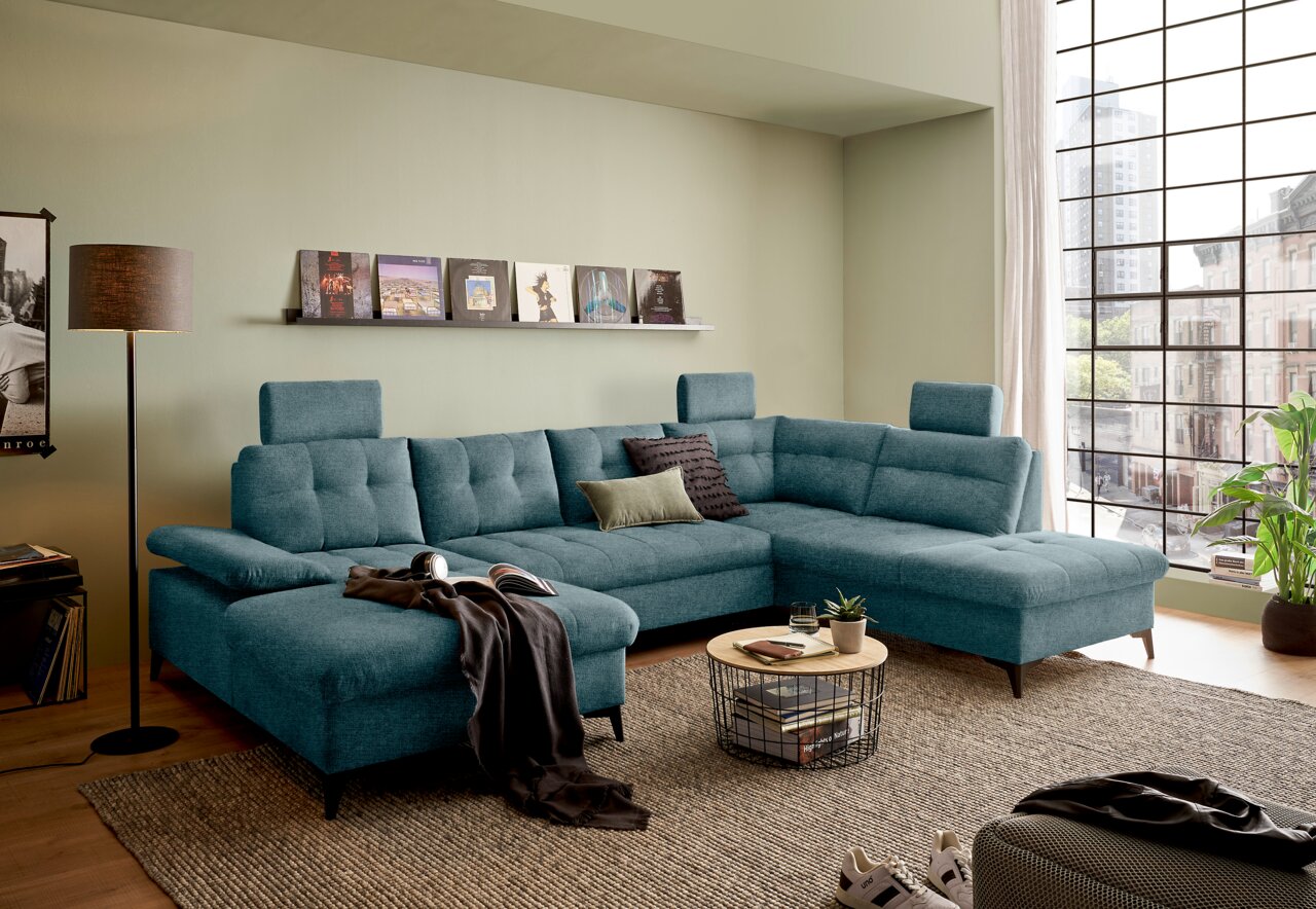 Moderne, türkisfarbene Rundecke in einem stilvollen Wohnzimmer mit großen Fenstern, aus der Perspektive von vorne links betrachtet.