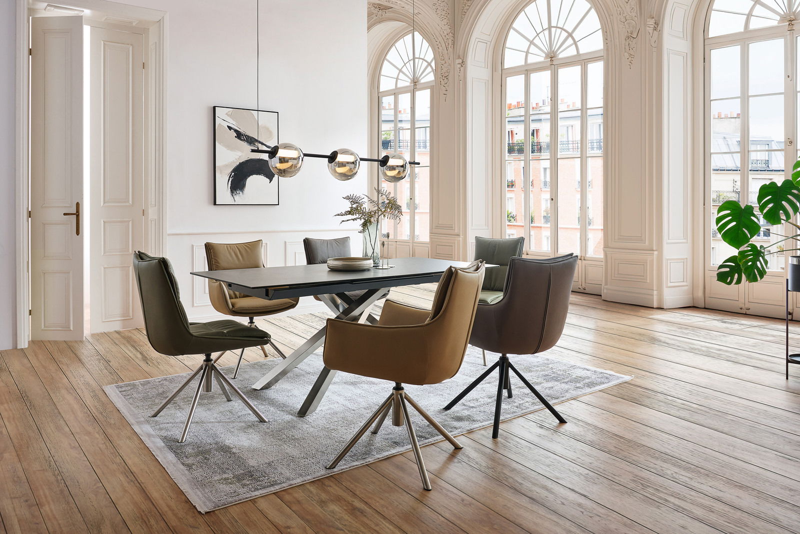 Esszimmer mit modernen Sesseln und Stühlen um einen rechteckigen Tisch, große Fenster im Hintergrund, seitliche Perspektive.