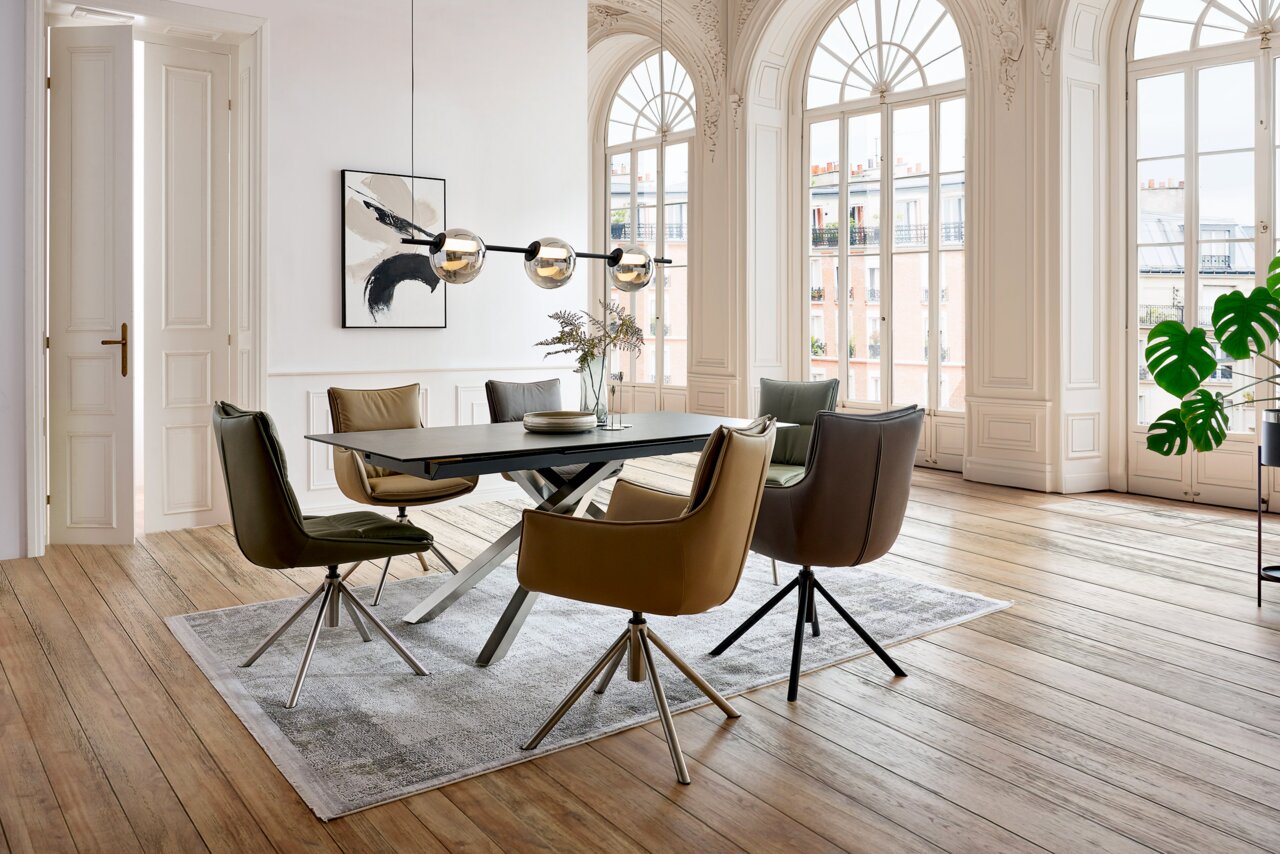 Novel Stuhl HOUSTON Esszimmer mit modernen Sesseln und Stühlen um einen rechteckigen Tisch, große Fenster im Hintergrund, seitliche Perspektive.