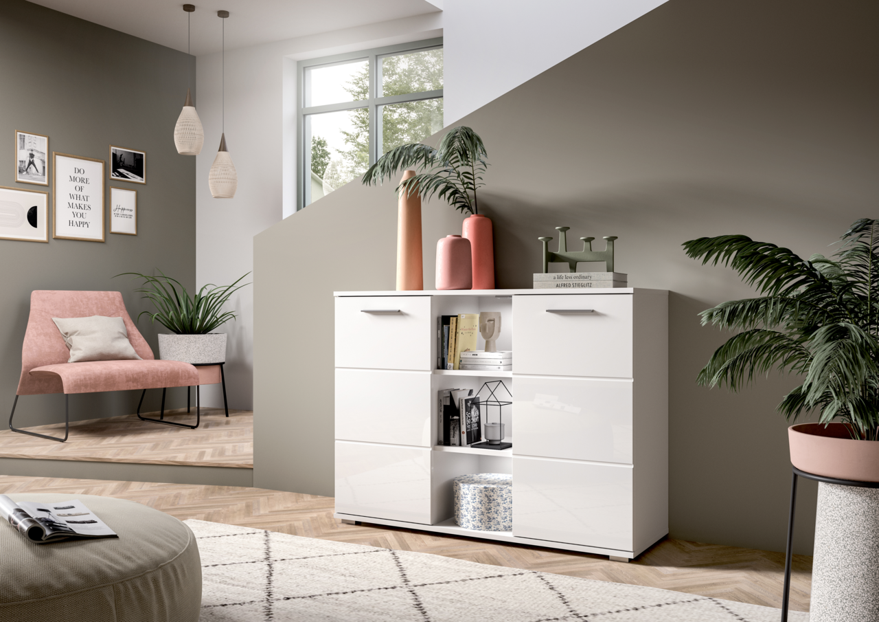 Moderne weiße Kommode mit glänzender Oberfläche, frontal fotografiert in einem stilvoll eingerichteten Wohnzimmer mit Pflanzen und Dekorationen.