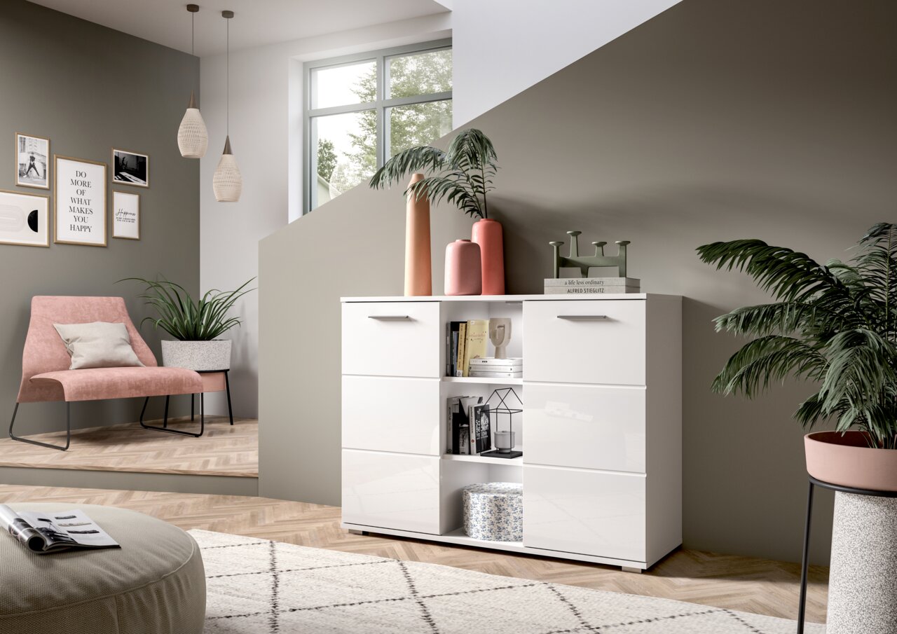 Moderne weiße Kommode mit glänzender Oberfläche, frontal fotografiert in einem stilvoll eingerichteten Wohnzimmer mit Pflanzen und Dekorationen.