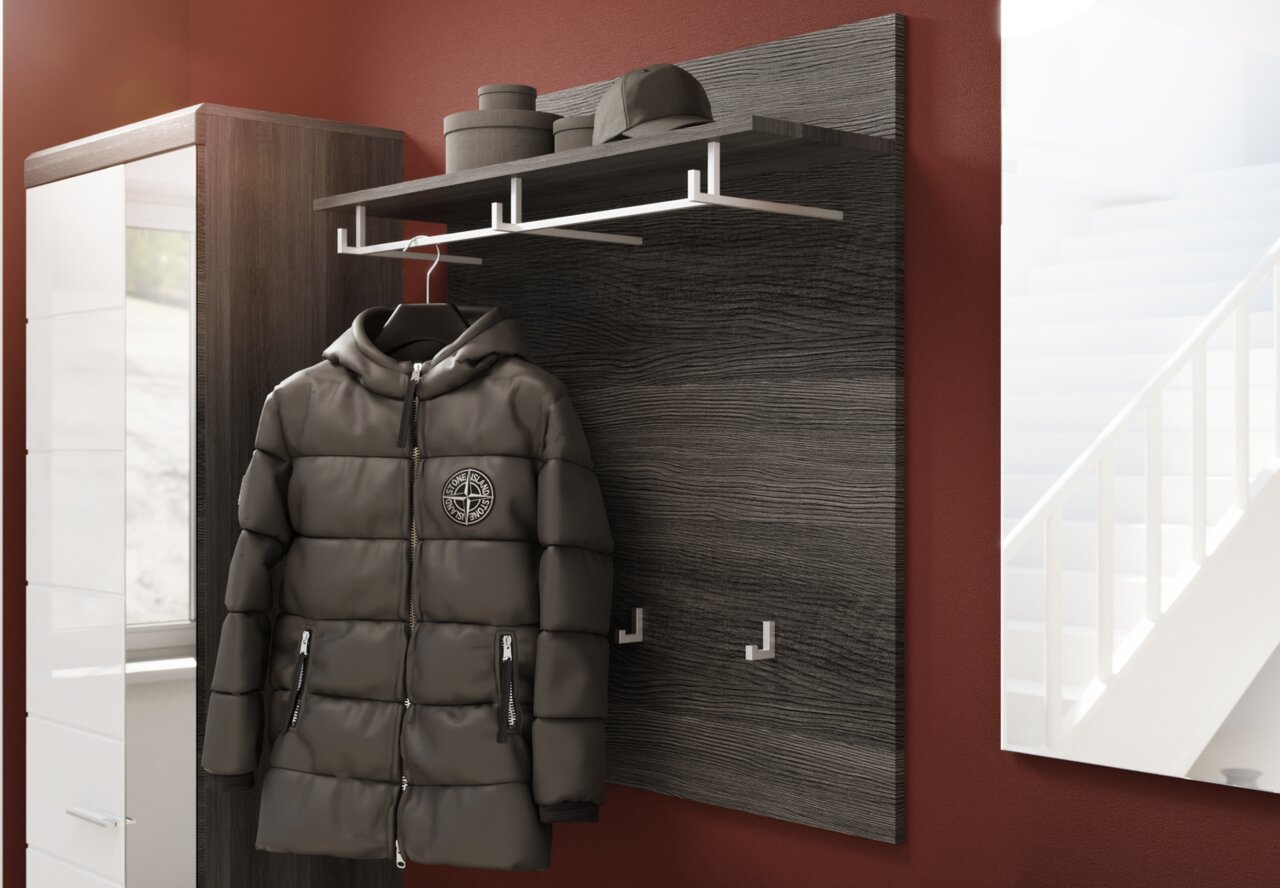 Garderoben-Set mit dunkler Holzoptik, bestehend aus einer Wandpaneele mit Haken und Ablage, darauf eine Jacke und Hüte. Perspektive von der Seite.