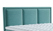 Close-up van een turquoise boxspringbed met een gestoffeerd hoofdeinde en een zichtbaar deel van de matras.