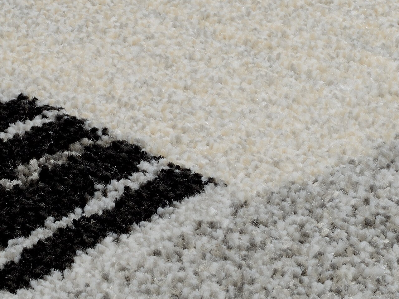 Nahaufnahme eines Teppichs mit geometrischem Muster in Schwarz, Weiß und Grau, perspektivisch von oben fotografiert.