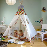 Zwei Kinder spielen in einem Tipi-Zelt mit farbiger Bemusterung, das in einem gemütlichen Kinderzimmer aufgestellt ist. Die Perspektive zeigt das Zelt von vorne, mit einem offenen Eingang.
