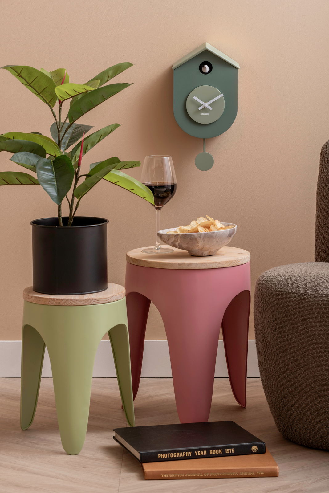 Grüne Wanduhr im Kuckucksuhren-Stil von KARLSSON, an einer beige gestrichenen Wand hängend, mit einem modernen, minimalistischen Design. Perspektive: Frontalansicht.