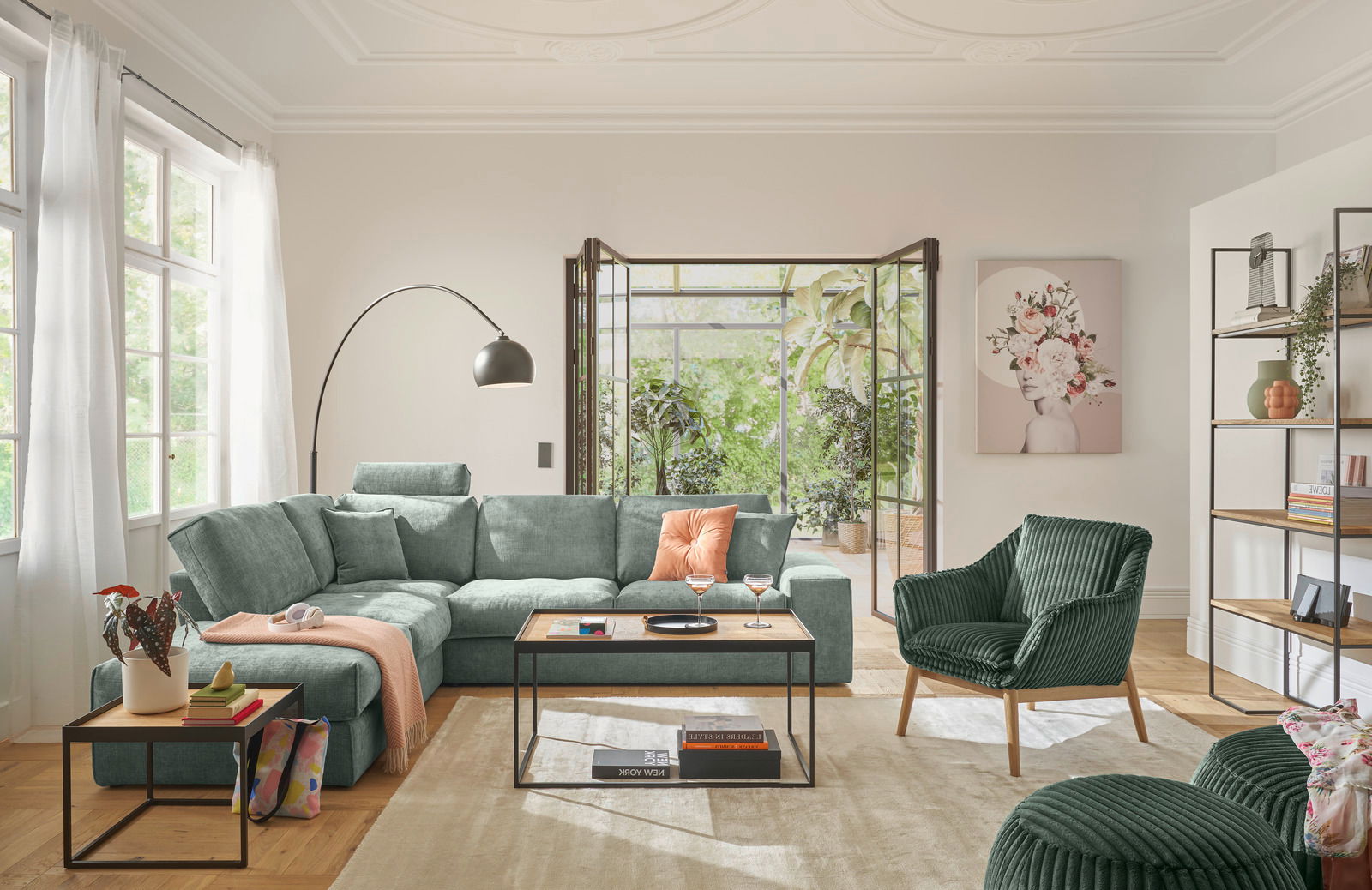 Gemütliches Wohnzimmer mit einer großen, grünen Rundecke, einem modernen Couchtisch und einem Sessel, aus der Perspektive von vorne betrachtet.