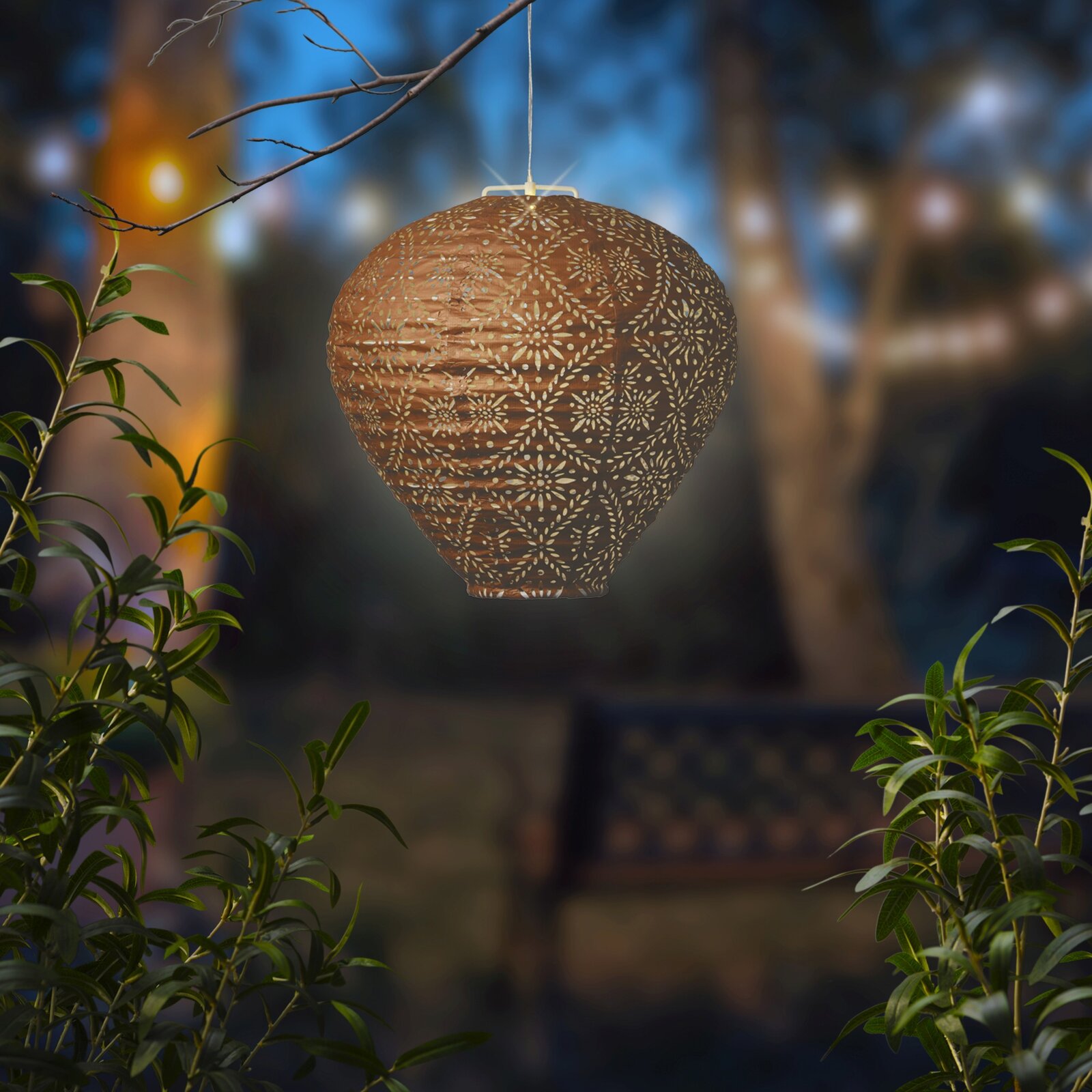 Hängende Solar Laterne mit filigranem Muster, beleuchtet in einem nächtlichen Garten, seitliche Perspektive