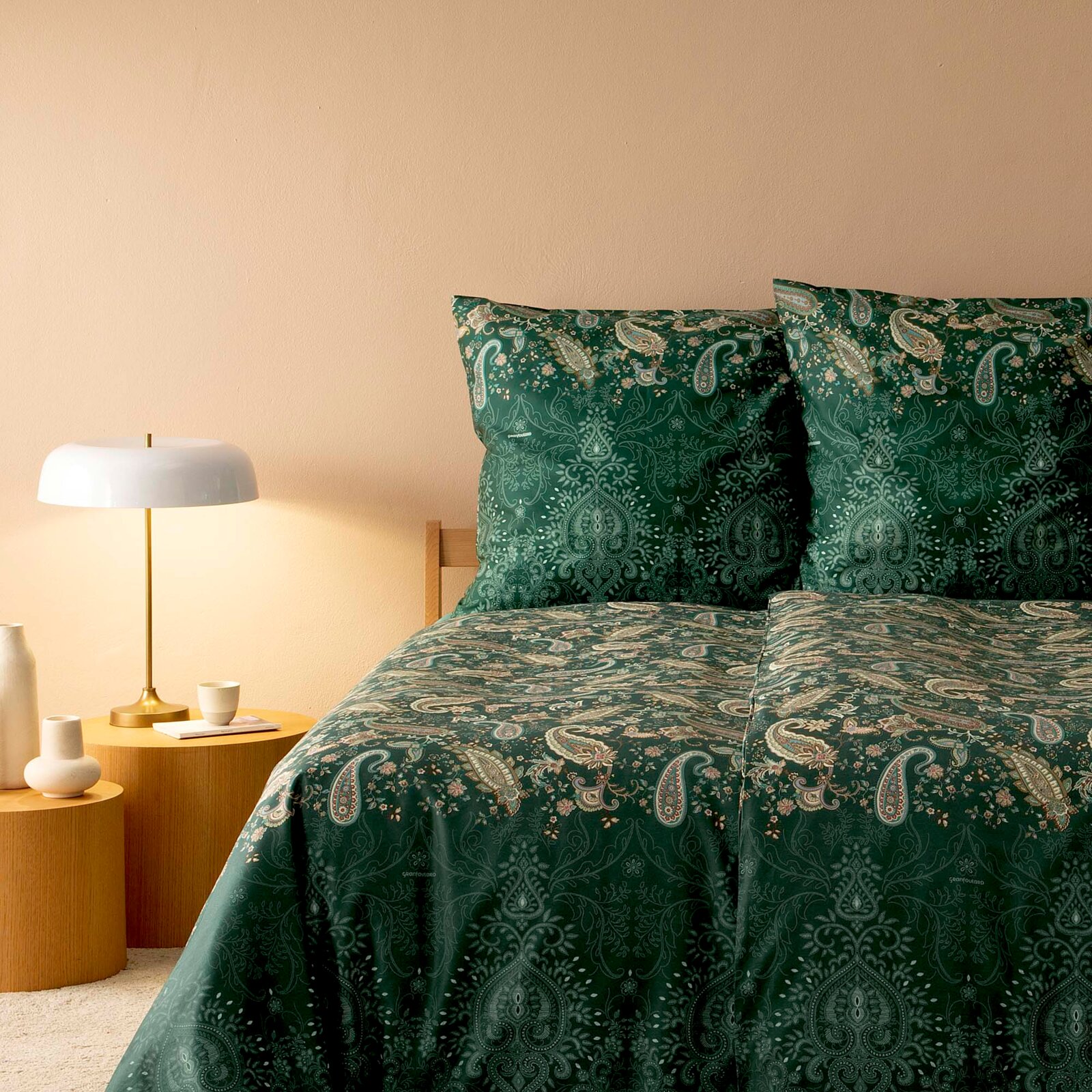 Bettwäsche-Set in elegantem Paisley-Muster in Grün- und Beigetönen, auf einem Bett mit zwei Kissen und einer Decke, seitliche Perspektive mit Nachttisch und Lampe.
