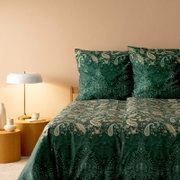 Bettwäsche-Set in elegantem Paisley-Muster in Grün- und Beigetönen, auf einem Bett mit zwei Kissen und einer Decke, seitliche Perspektive mit Nachttisch und Lampe.