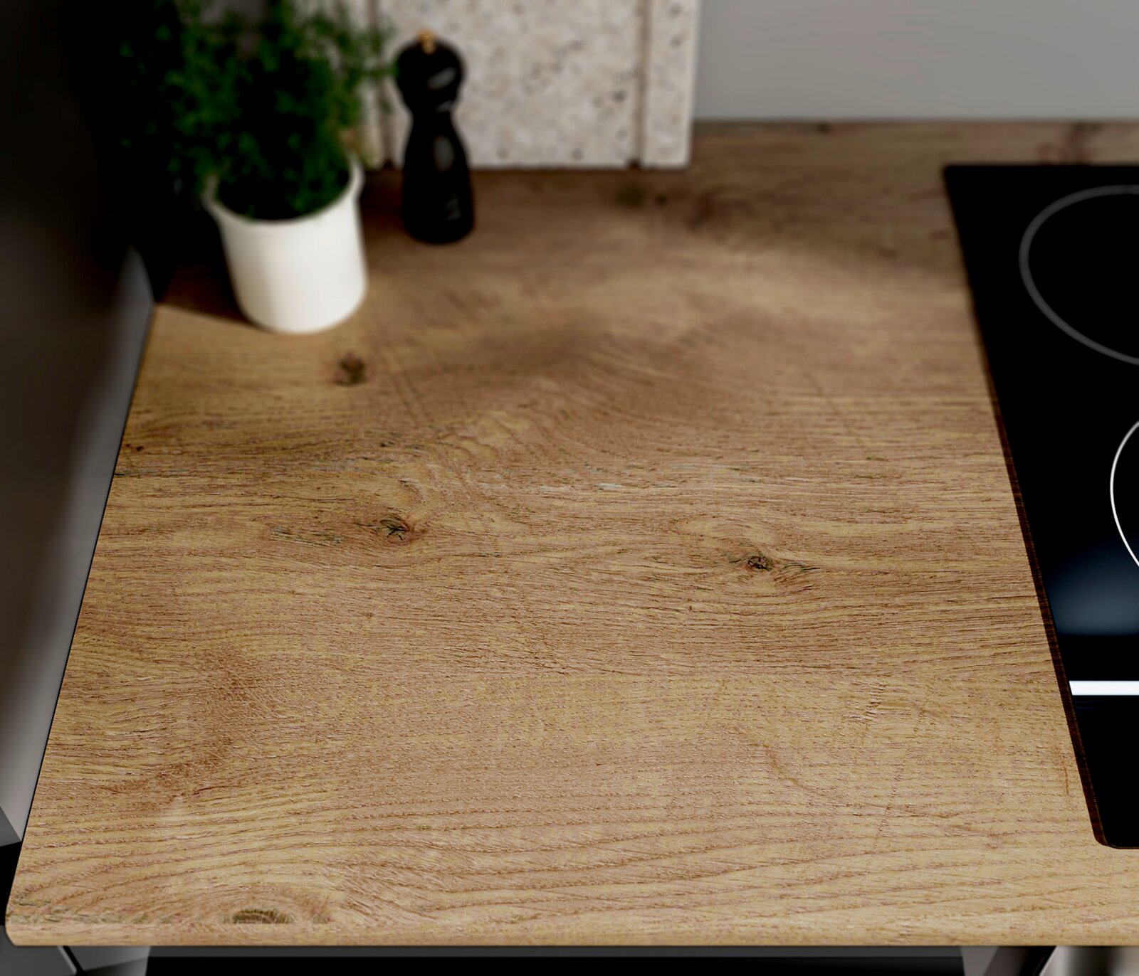 Holz-Arbeitsplatte in Eichenoptik in einer modernen Küche, Draufsicht aus leicht schräger Perspektive; im Hintergrund Kräutertopf und Pfeffermühle, rechts ein schwarzes Kochfeld